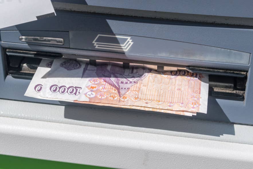 Icelandic krona banknote being dispensed from an ATM, illustrating cash withdrawal in Iceland.