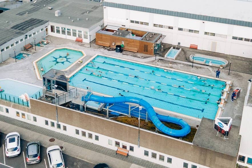 Outdoor geothermal swimming pool complex in Reykjavik, Iceland, with lap pool, hot tubs, and waterslide.