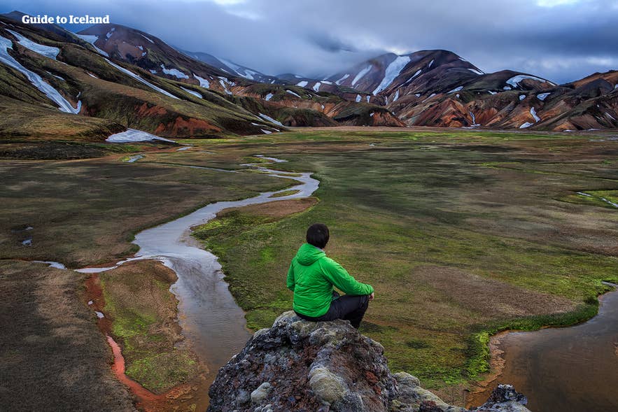 Una persona con giacca verde seduta su una roccia che osserva le montagne colorate di Landmannalaugar, Islanda. Una persona con giacca verde seduta su una roccia che osserva le montagne colorate di Landmannalaugar, Islanda.