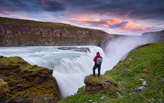 A tourist stands on the edge of a cliff overlooking the cascade of Gullfoss Waterfall.