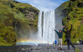 A couple poses for a photo in front of Skogafoss Waterfall in Iceland.