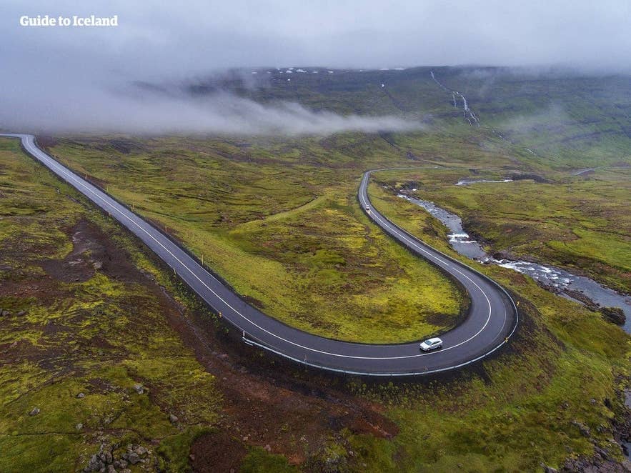 Car driving on a winding Ring Road stretch in misty mountains, a classic road trip scene in Iceland in April.
