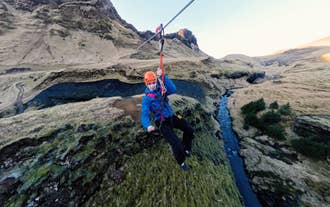 Zipliner in a blue jacket crossing a canyon above a river near Vik on Iceland South Coast