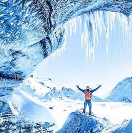 アイスランドの氷の洞窟の入り口で、両手を広げて立つ人物と周囲の絶景。