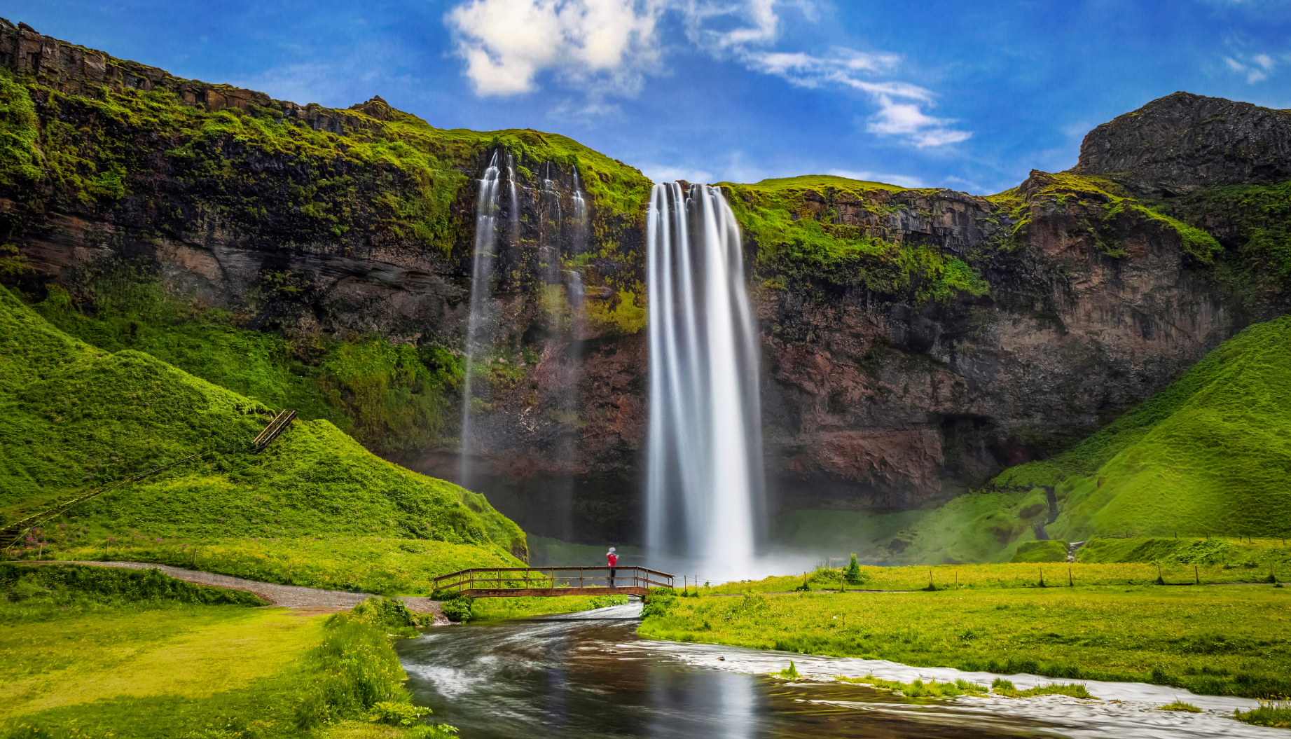 Der Seljalandsfoss-Wasserfall stürzt über eine grüne Klippe an der Südküste. Hinter dem Wasserfall führt ein Weg entlang.