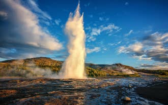 Strokkur geyser erupting in a powerful column of steaming water under a blue sky in a geothermal valley in Iceland