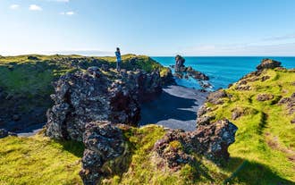Traveler standing on lava rocks above Djupalonssandur Black Pebble Beach on a Snaefellsnes Peninsula day tour in Iceland.