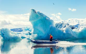 A guide driving a small boat past icebergs in Jokulsarlon Glacier Lagoon with Vatnajokull Glacier in the background