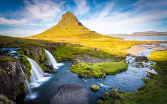 Kirkjufell Mountain and Kirkjufellsfoss Waterfall glow in golden light on Snaefellsnes Peninsula.