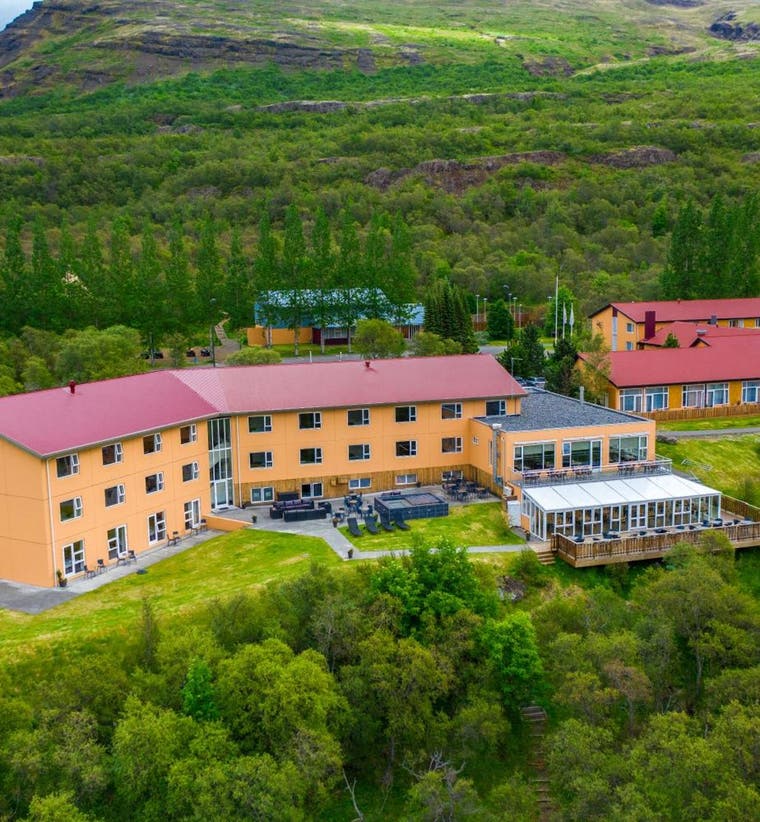 3-star hotel complex in Iceland with red roofs, surrounded by green hills, trees, and scenic countryside views.