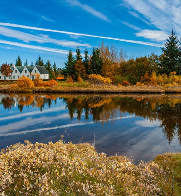 Thingvellir National Park under a clear blue sky, with autumn foliage surrounding a calm body of water.