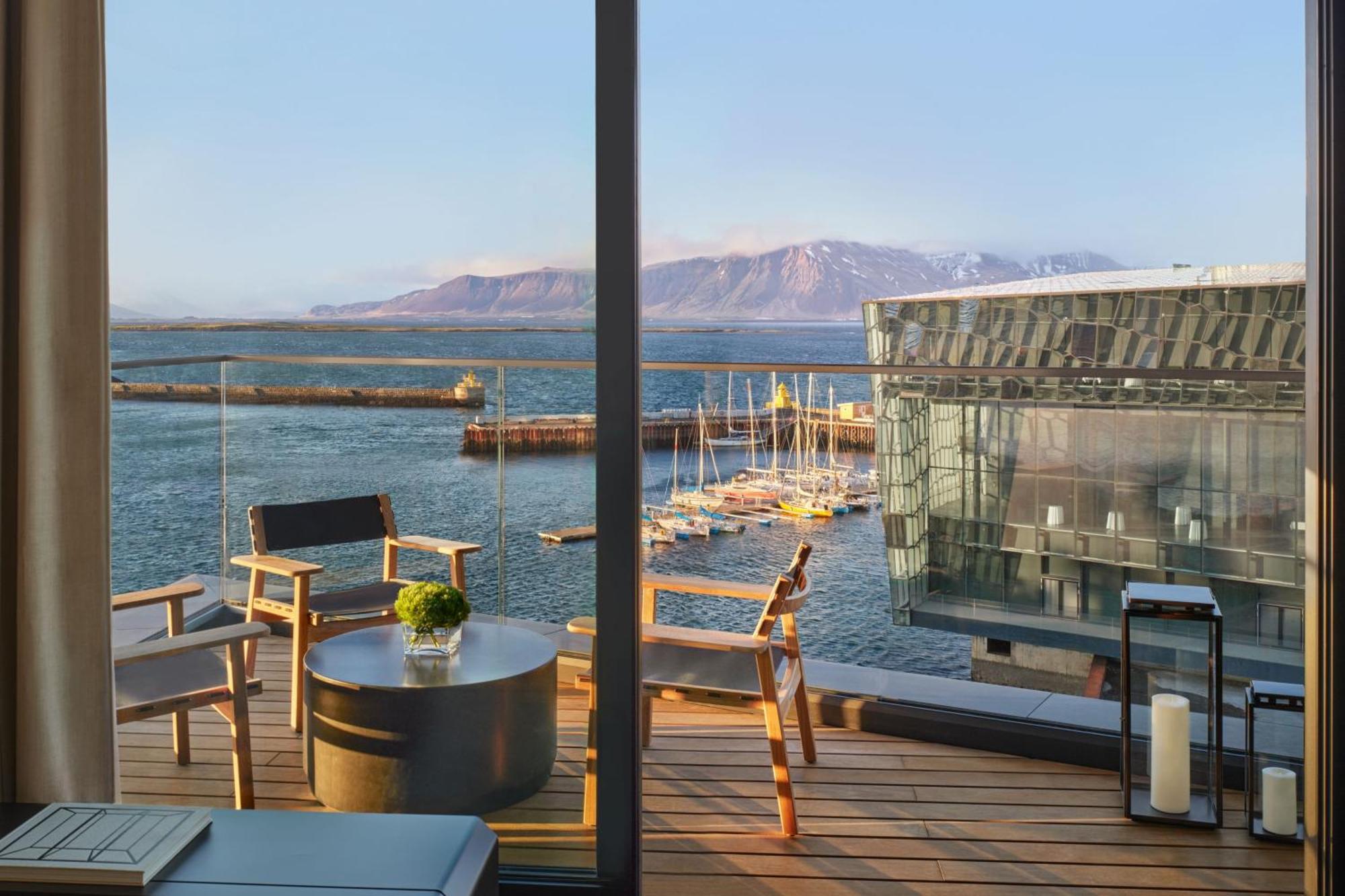 Modern 5-star hotel balcony in Reykjavik overlooking the harbor and Harpa Concert Hall with ocean and mountain views.