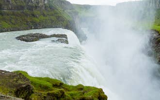 Powerful white water and rising mist tumble over the mossy green ledge of Gullfoss Waterfall.