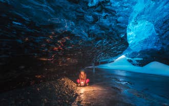 Blauwe ijsgrot in de Vatnajökullgletsjer in IJsland met een reiziger die een verlichte gletsjertunnel verkent.