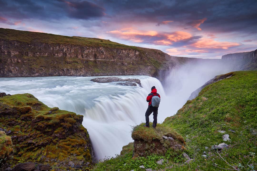 Gullfoss-vandfaldet i Island med en rejsende på en seks dages Ringvejen-rute, der står ved den brusende gletsjerflod i kløften.
