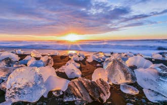 Diamond Beach with ice chunks on black sand at sunrise in South Iceland as viewed during a Ring Road tour.