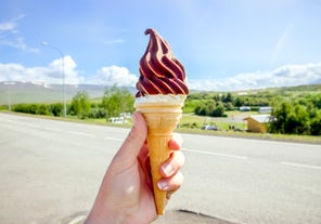 Hand holding tasty Icelandic local soft serve vanilla ice cream dipped in hot chocolate, with Iceland nature in the background.