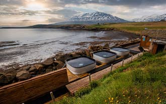Outdoor beer spa hot tubs overlooking fjord and mountains in North Iceland at sunset.