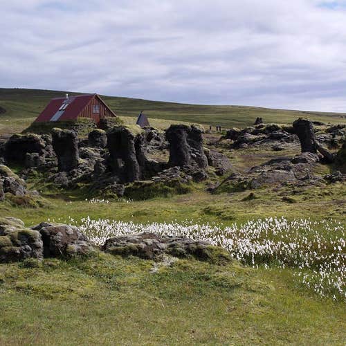 A picturesque meadow and rugged, rocky terrain surrounding a mountain hut in the Icelandic Highlands.