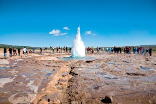 People watch as the Strokkur geyser erupts high in the air at the Geysir geothermal area in the Haukadalur valley.