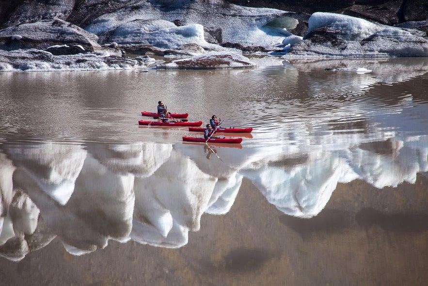 Kayakistas remando en la laguna del glaciar S&oacute;lheimaj&ouml;kull en el sur de Islandia, rodeados de formaciones de hielo y vistas al glaciar.
