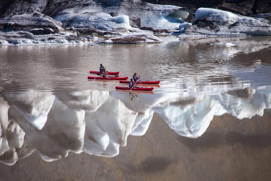 Des kayakistes pagaient sur la lagune du glacier Solheimajokull, dans le sud de l’Islande, entourés de formations de glace et de paysages glaciaires.