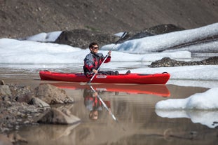 A person kayaks in between icebergs on the serene waters below the Solheimajokull glacier.