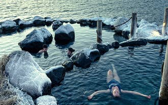 Une personne flotte sur le dos, se relaxant dans l'une des bassins naturels des sources d'eau chaude de Hvammsvik.