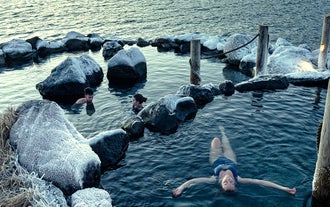 Une personne flotte sur le dos, se relaxant dans l'une des bassins naturels des sources d'eau chaude de Hvammsvik.