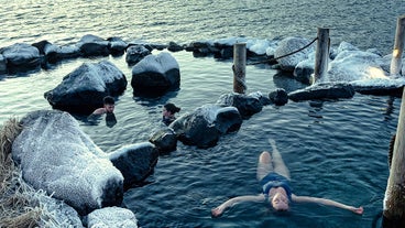 A person floats on their back, relaxing in one of the natural hot pools at the Hvammsvik Hot Springs.