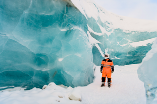 A person wearing a snowmobiling suit and helmet stands on the Langjokull glacier next to a massive ice wall.