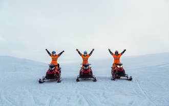 Des personnes conduisant des motoneiges sur le glacier Langjokull s'arrêtent pour une photo, les bras en l'air, au milieu d'une vaste étendue glacée.