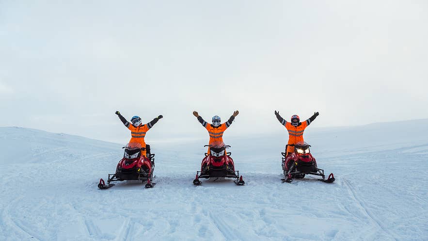 Three snowmobilers on a glacier with their arms raised