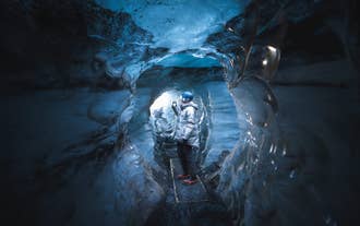 A traveler explores a tunnel inside a blue ice cave inside Vatnajokull Glacier on a multi-day Iceland tour.