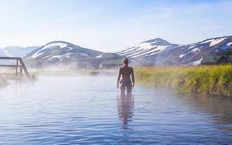 Traveler bathing in natural hot spring river in Landmannalaugar with colorful mountains in background.
