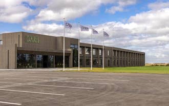 Hotel Loa presents a modern exterior with a clean facade, parking area, and a cloudy Icelandic sky.