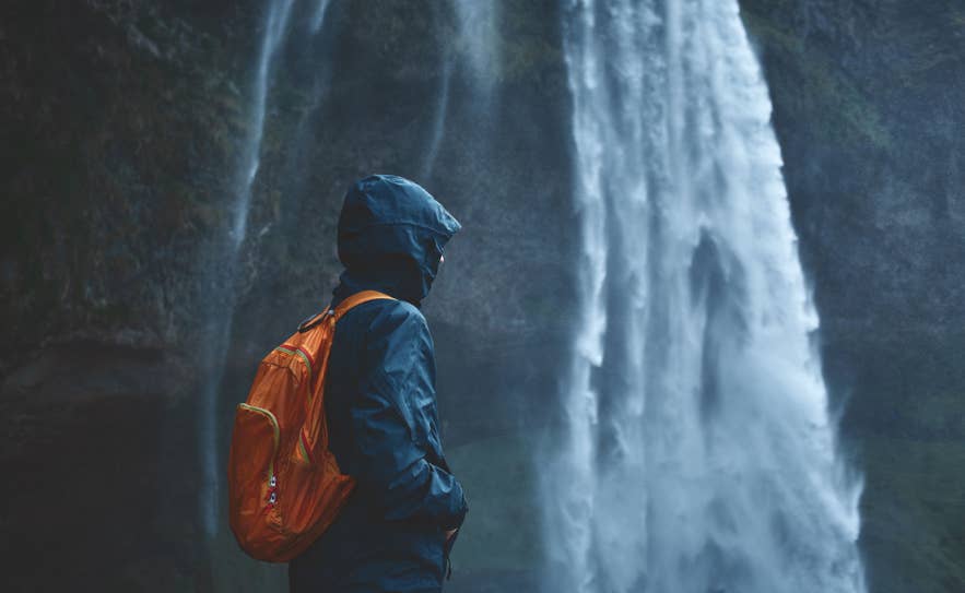 Traveler with backpack standing near dramatic waterfall in Iceland.