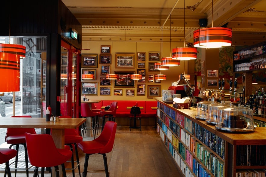 Interior of The Laundromat Café in Reykjavik with red chairs, bookshelves, and framed photos on the wall.