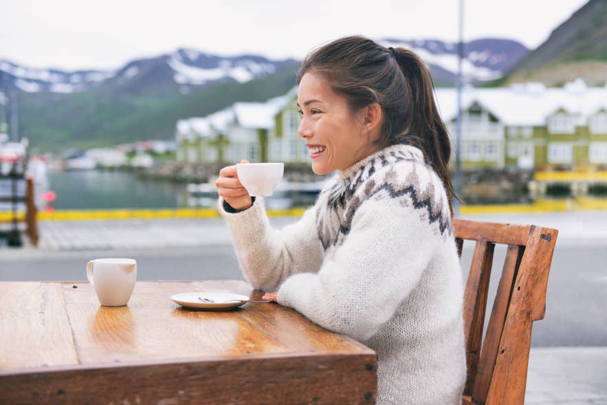Traveler in lopapeysa sipping coffee at an outdoor cafe.