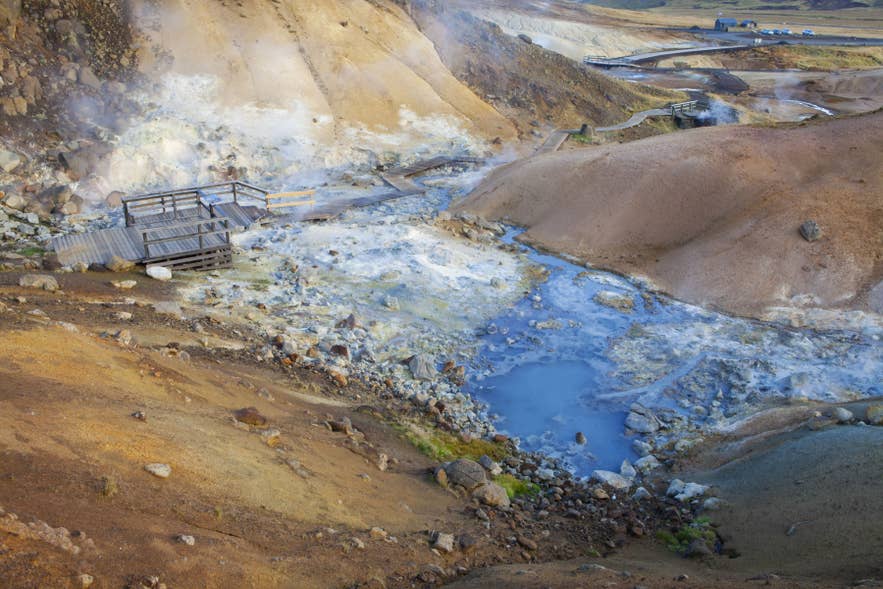 Wooden boardwalk over steaming mud pools and mineral-rich terrain in the Hverir geothermal area, Iceland.