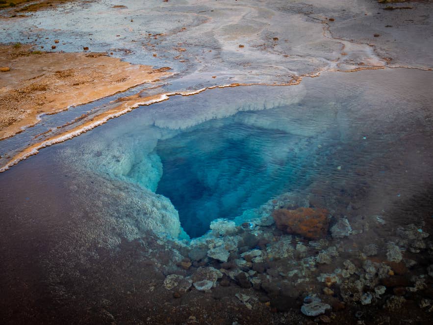 Close-up of a deep blue hot spring at Strokkur geyser in the Haukadalur geothermal area, Iceland, with mineral deposits along the edges.