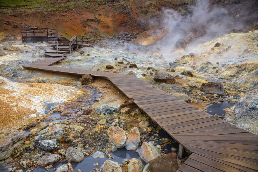 Wooden boardwalk winds through steaming mud pools and colorful geothermal terrain at Hverir near Namafjall, Iceland.