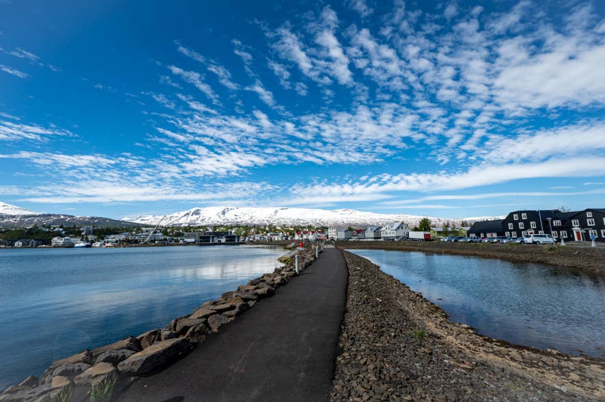 Coastal path in Akureyri overlooking the calm fjord waters and snow-capped mountains under a bright blue sky.
