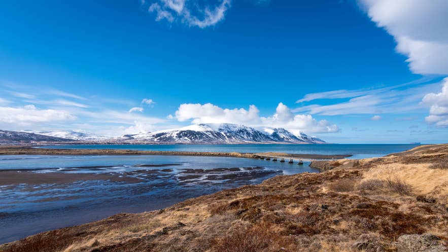 Panoramic view of Skagafjordur fjord in North Iceland, featuring snow-capped mountains and a bridge over blue waters.