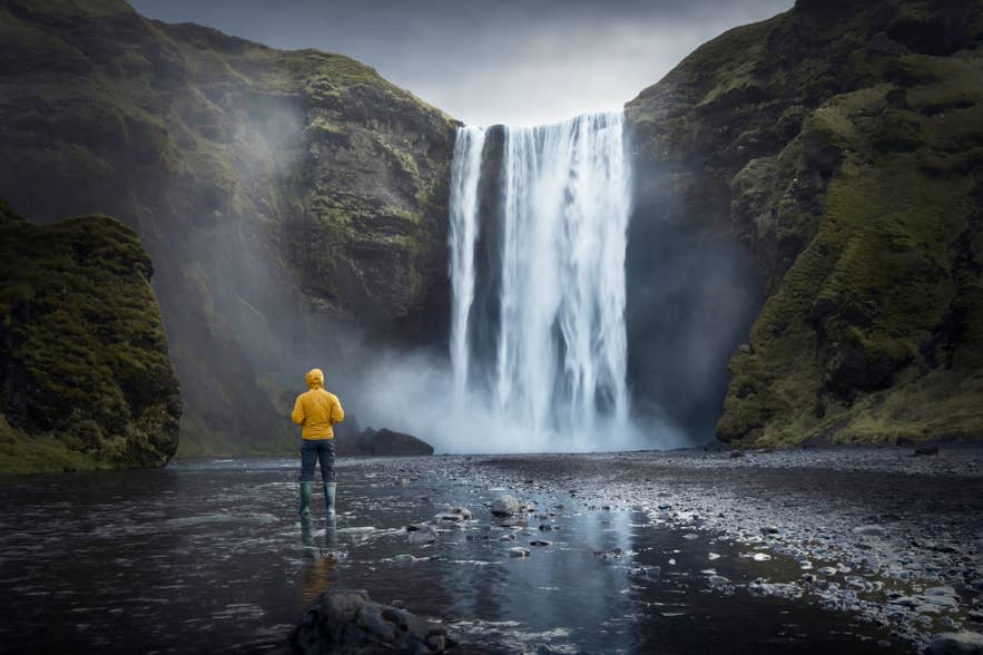 นักท่องเที่ยวยืนอยู่ที่น้ำตก Skogafoss ทางตอนใต้ของไอซ์แลนด์ ท่ามกลางละอองน้ำและหน้าผา