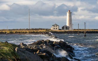 Waves crash against a rocky breakwater leading toward Grotta Lighthouse on the Seltjarnarnes Peninsula.