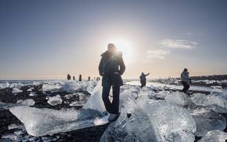 A traveler poses for a photo along the gem-like ice chunks of Diamond Beach.