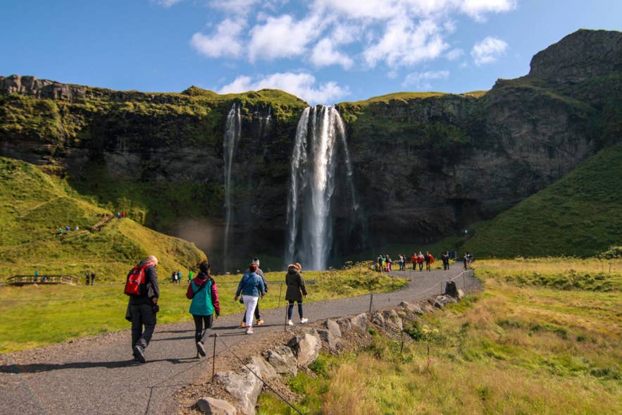 Visitors walking along the path beside Seljalandsfoss Waterfall in South Iceland.