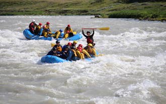 Rafting team rides strong rapids on Hvita River, paddles raised as waves crash.