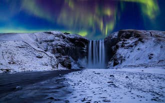 Aurora boreale sopra la cascata Skógafoss circondata dalla neve nel sud dell'Islanda.